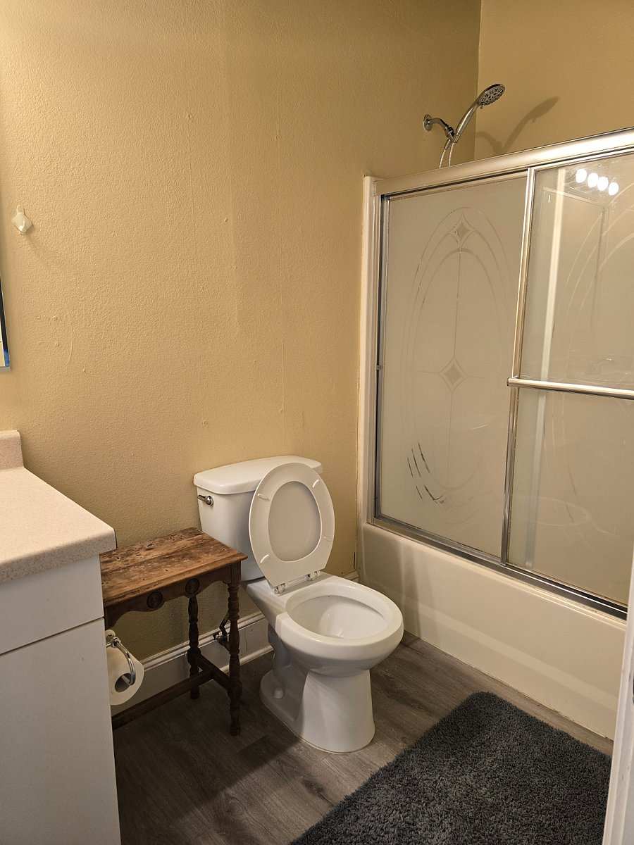 Studio 105 bathroom: a toilet beside a tub with frosted sliding doors and a rain shower head.