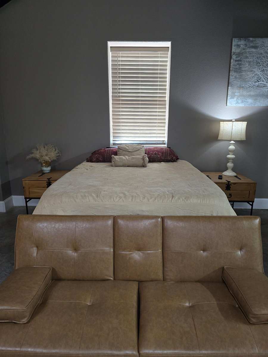 Studio 204: a bed with two bedside lamps under a window, a tan leather futon at its foot.